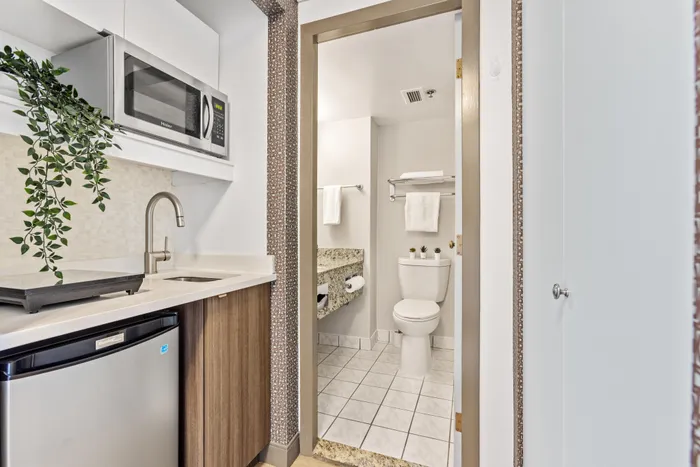 Chic and compact apartment interior featuring a modern kitchenette with stainless steel appliances and a view into a sleek tiled bathroom.