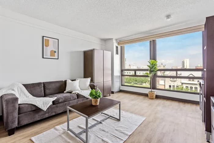 Bright living room with a plush gray sofa, large window offering stunning city views, and stylish hardwood flooring.